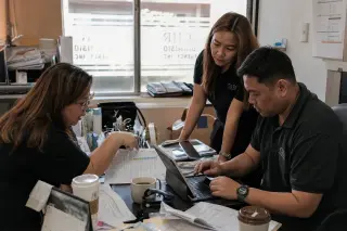 CHR team in a cluttered back office discussing documents intently, focused on insurance paperwork amid a natural working atmosphere.