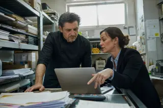Restaurateur and advisor in a storage room, absorbed in reviewing documents together by daylight, authentic workplace atmosphere.